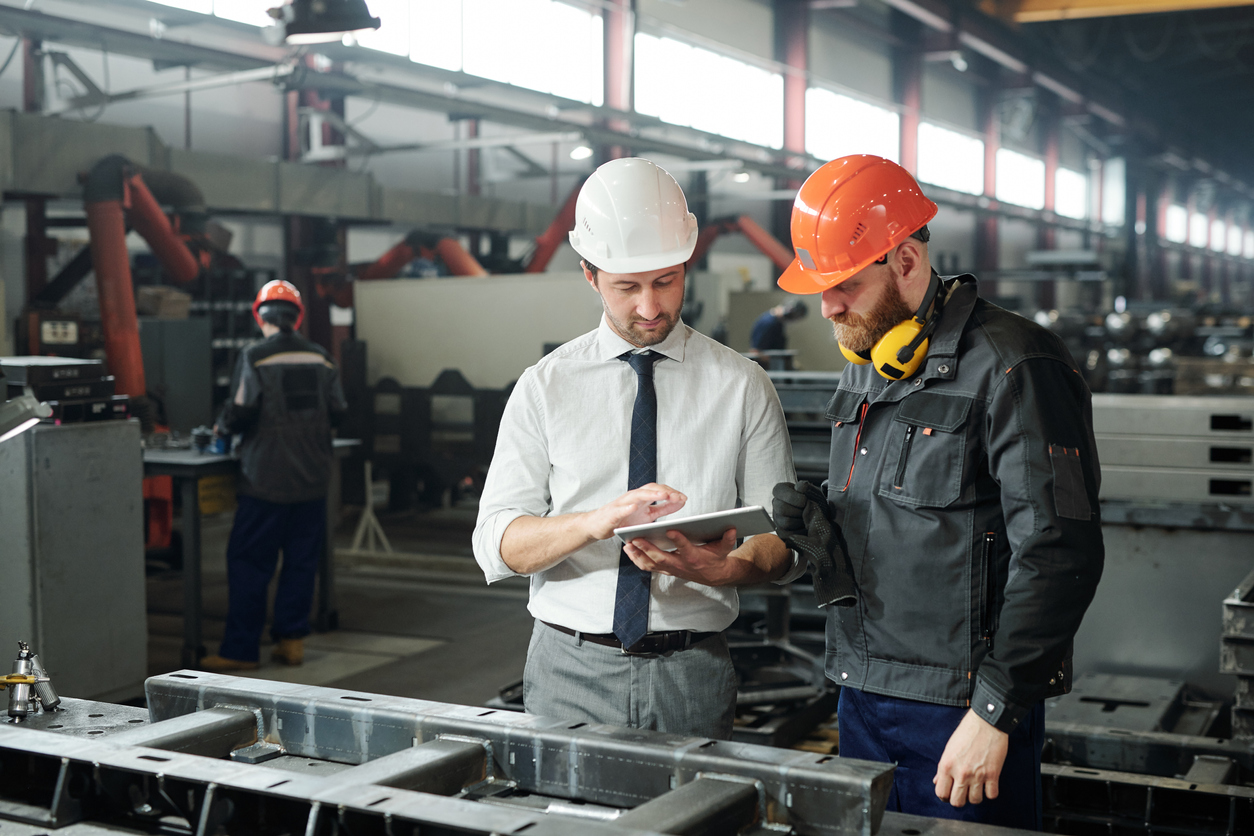 Young man in hardhat and bearded engineer discussing technical sketch