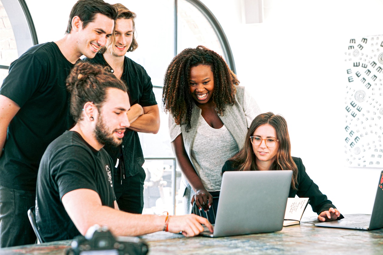 Employees gathered around a laptop computer laughing and smiling